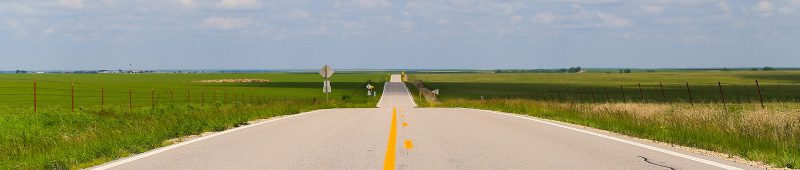 Pictured: Kansas road in the plains with green grass.