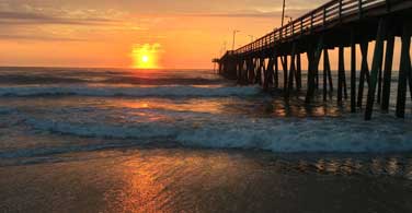 Pictured: A pier leading out to the ocean under a sunset in Virginia Beach Virginia.